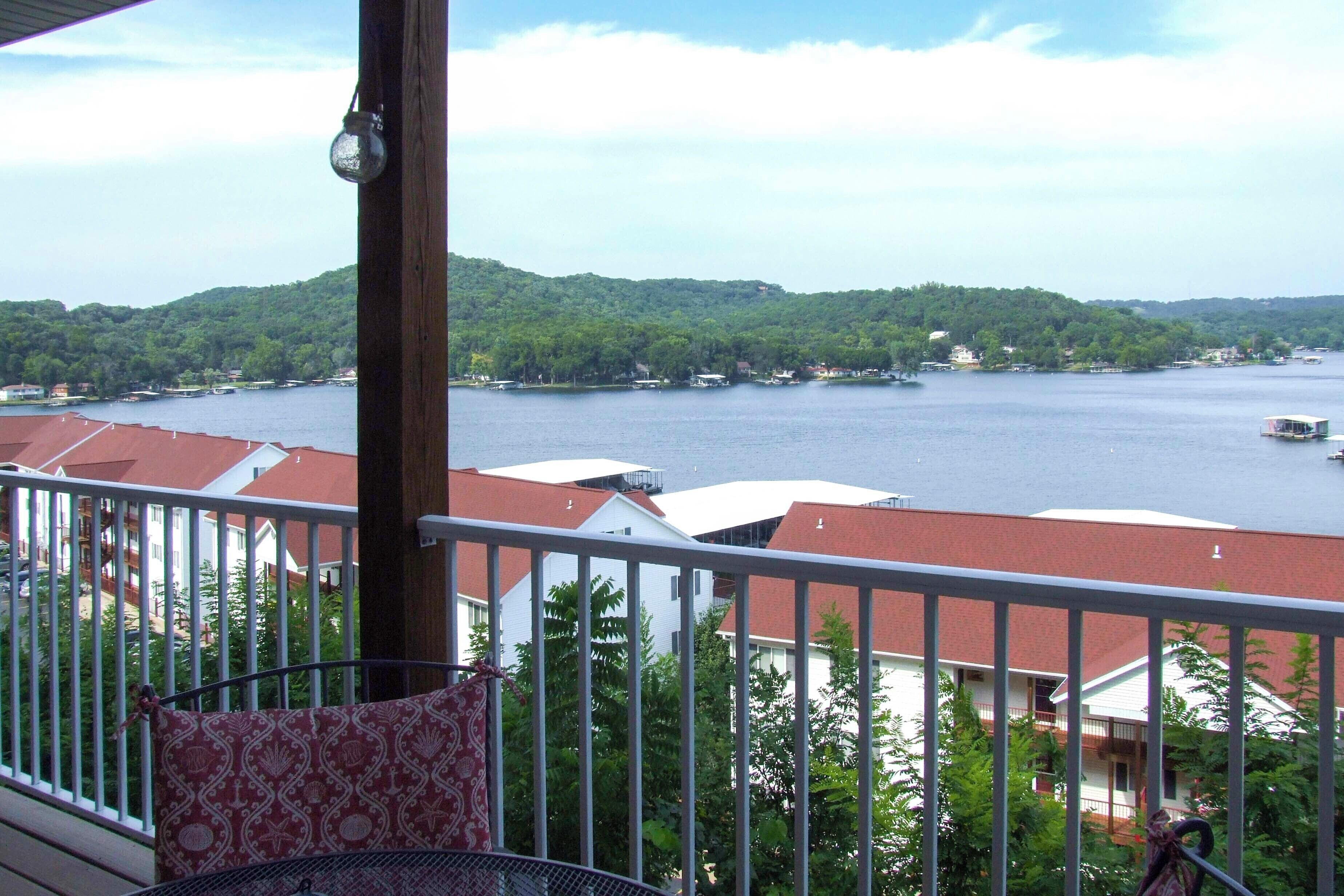 A balcony with a view of a lake, surrounded by greenery and buildings.
