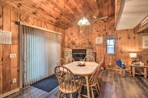 A wooden interior with a dining table, chairs, a fireplace, and a ceiling fan. - Lakeview Forest Cabin w/ Deck < 1/2 Mile to Beach! (Madison)