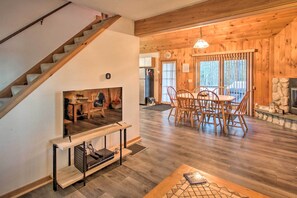 Een houten interieur met een trap, een eethoek met een tafel en stoelen, een open haard en een televisie op een standaard.