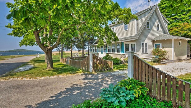 A two-story house with a covered porch, a fenced yard, and a view of the water. - Common Fence Point Cottage w/ Ocean Views! (Portsmouth)