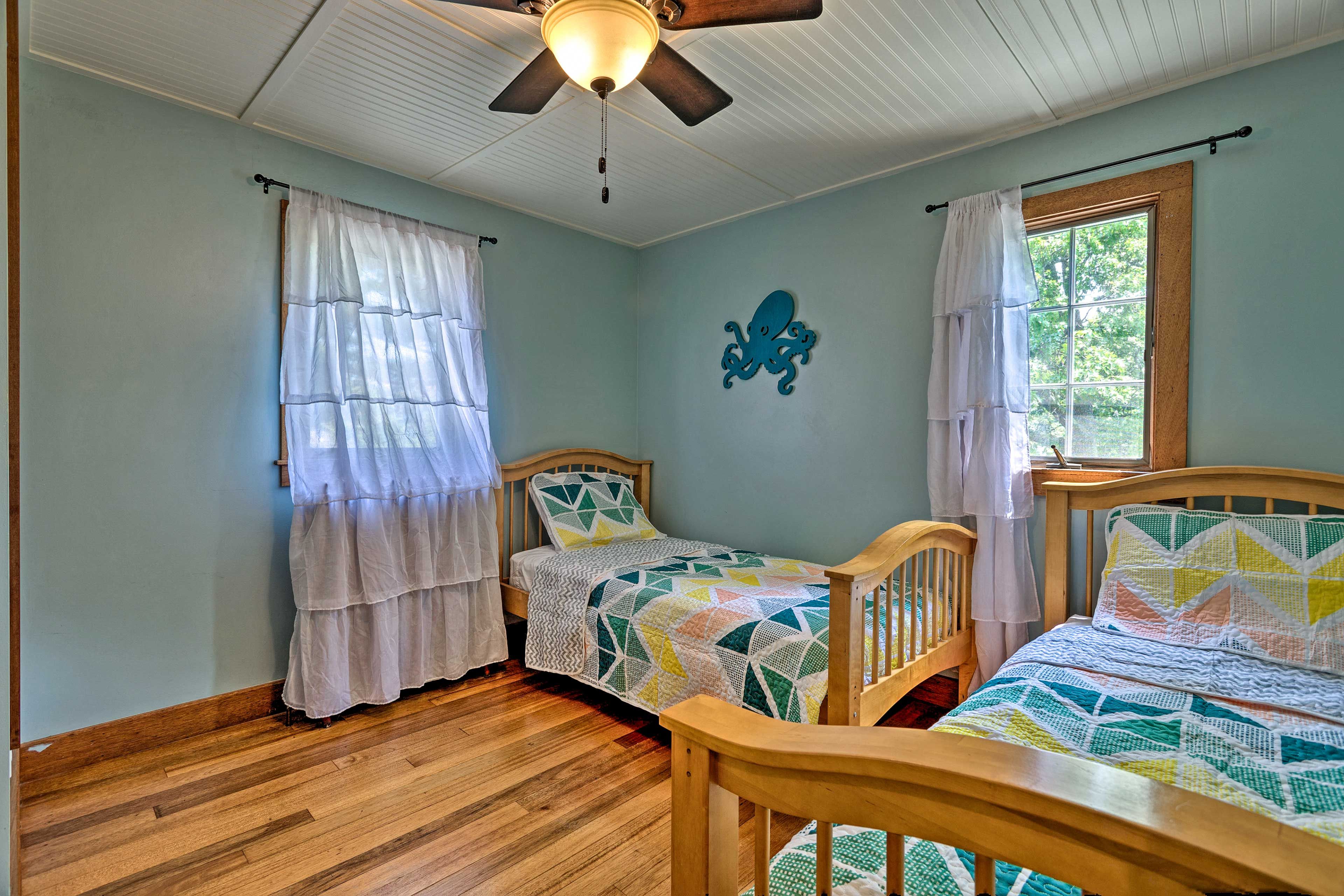 A bedroom with two wooden beds, a ceiling fan, and a window with curtains.