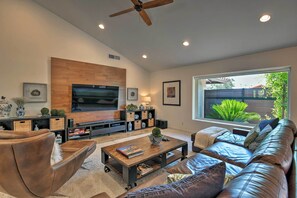 Una sala de estar moderna con un televisor de pantalla plana grande, sofás de cuero, una mesa de centro y un ventanal con vistas a zonas verdes.