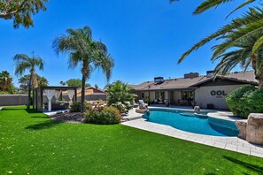 Un patio trasero con piscina, palmeras y un área de estar techada.