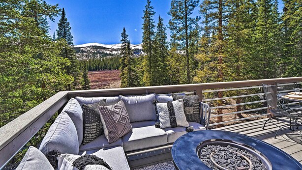 Une terrasse avec un canapé et des fauteuils, offrant une vue sur une forêt et une montagne dont le sommet est enneigé.