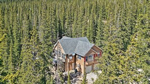 Une cabane en rondins à deux étages, dotée d’un toit en pente et entourée d’une forêt dense.