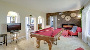 Une table de billard dans un salon, avec un téléviseur, un canapé et une cheminée.