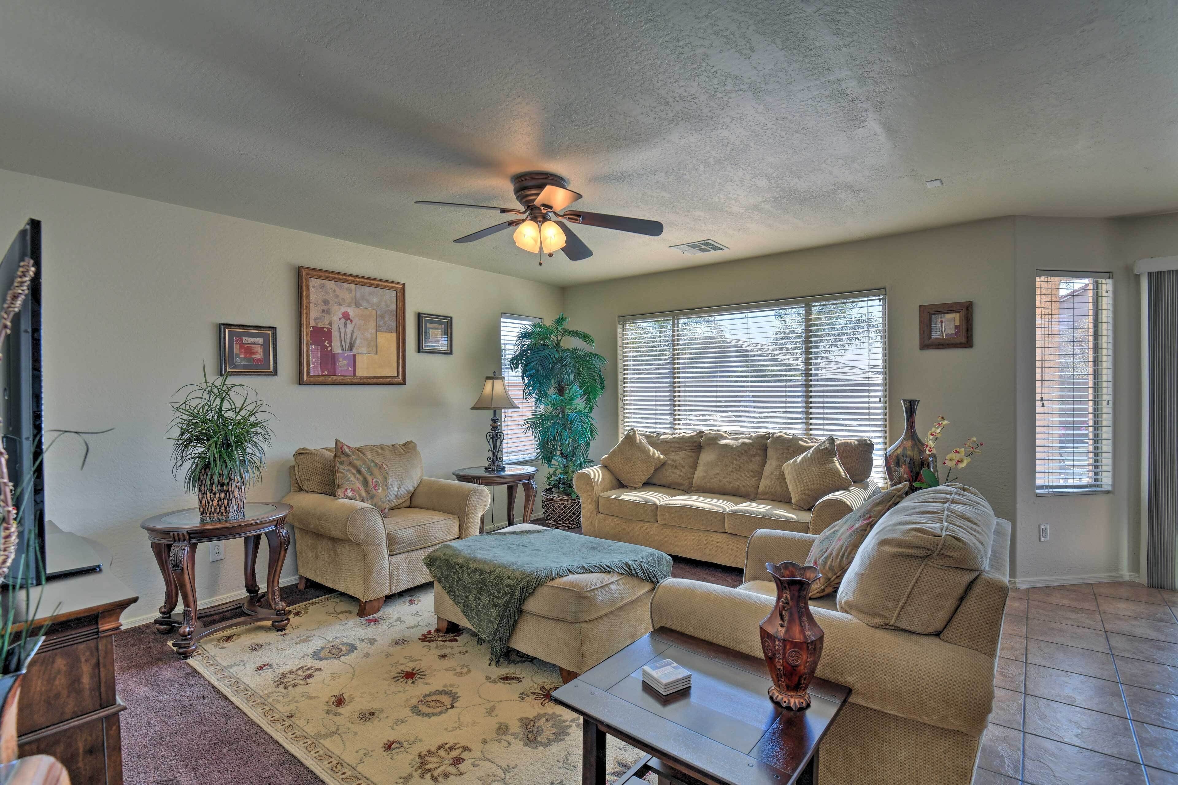 A spacious living room with a ceiling fan, two couches, a coffee table, and a large window with blinds.