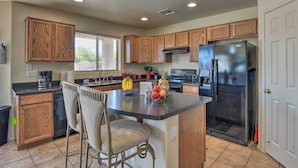 A kitchen with wooden cabinets, a central island with chairs, a refrigerator, and a stove. - Private Pool & Hot Tub: San Tan Valley Home (San Tan Valley)