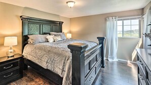 Un dormitorio con una cama grande, mesitas de noche, un aparador y una ventana con cortinas.