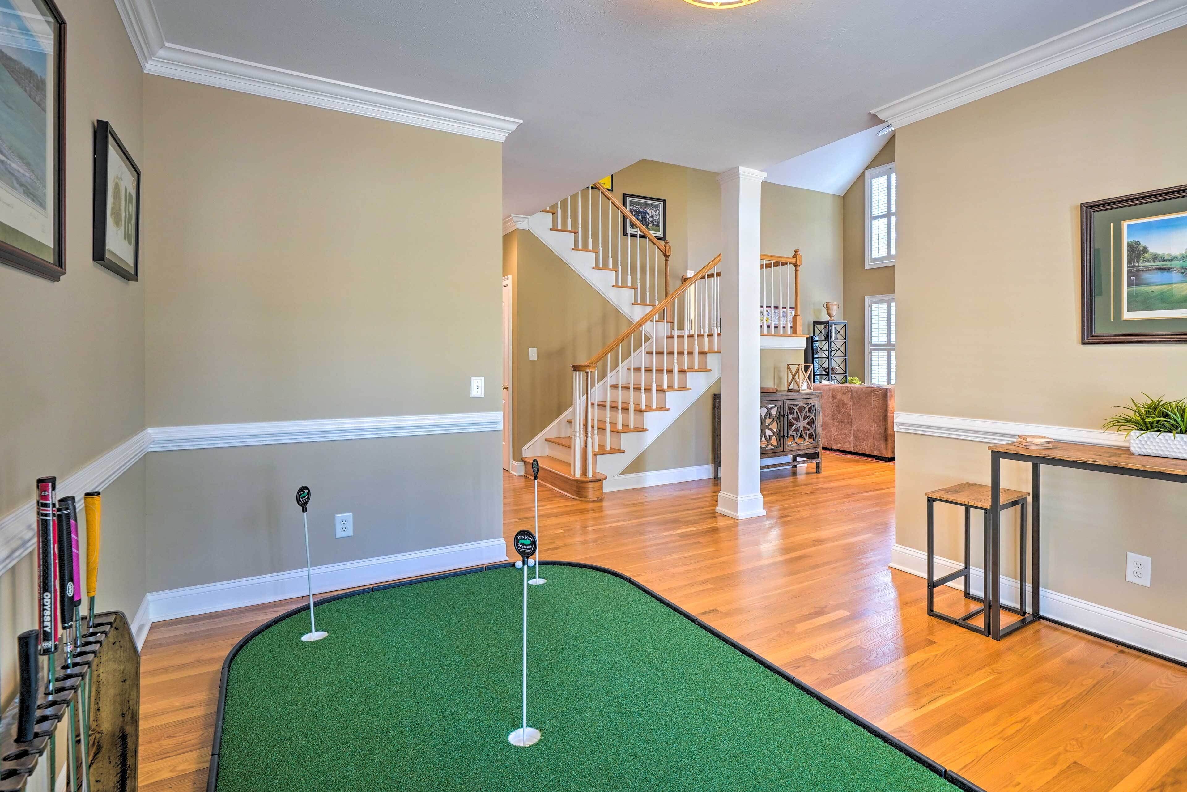 A home interior with a green artificial turf area, wooden flooring, a staircase, and a dining area with a table and chairs.