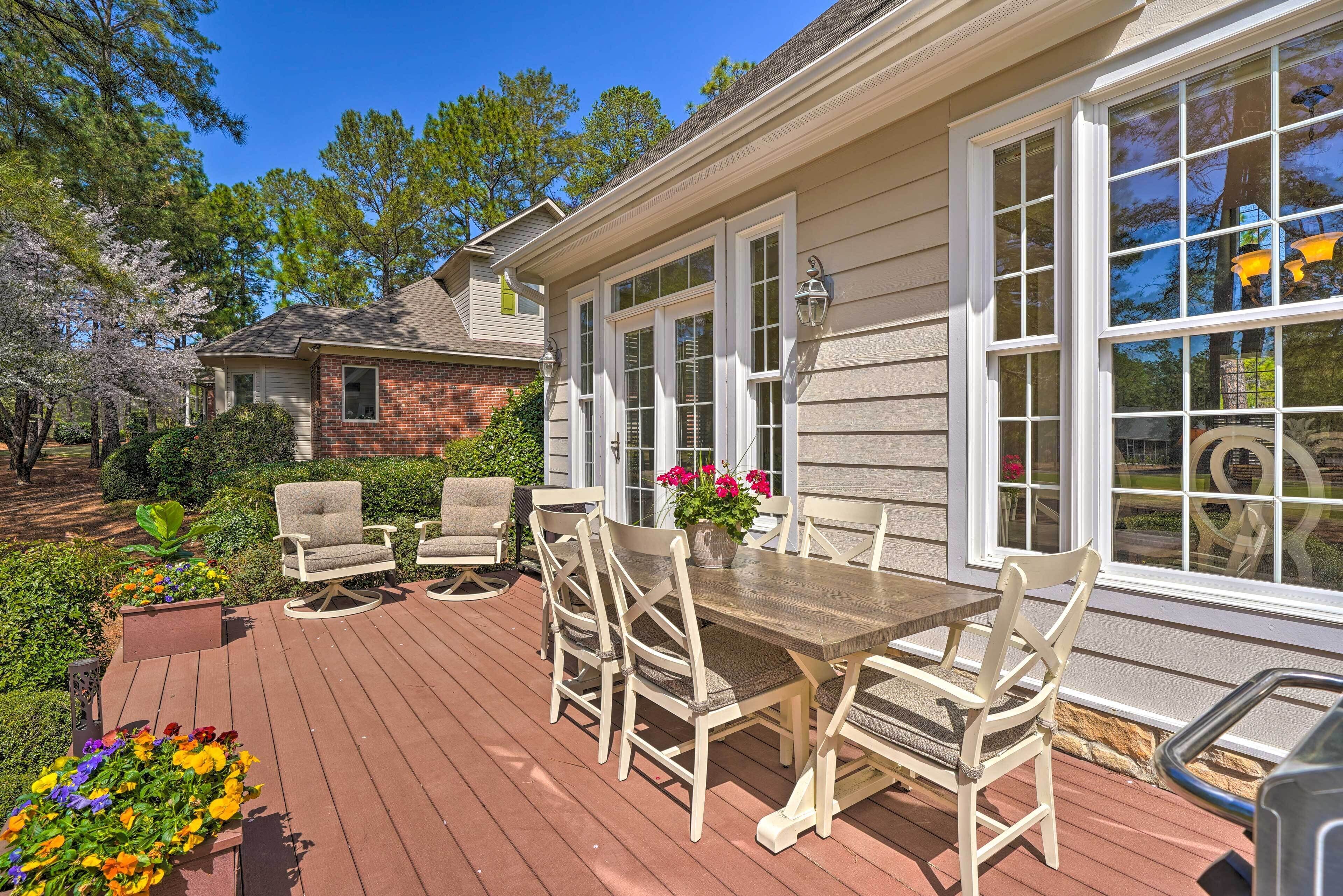 A wooden deck with outdoor furniture, a brick house in the background, and a clear blue sky.