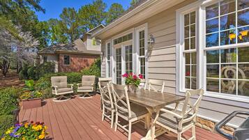 A wooden deck with outdoor furniture, a brick house in the background, and a clear blue sky.