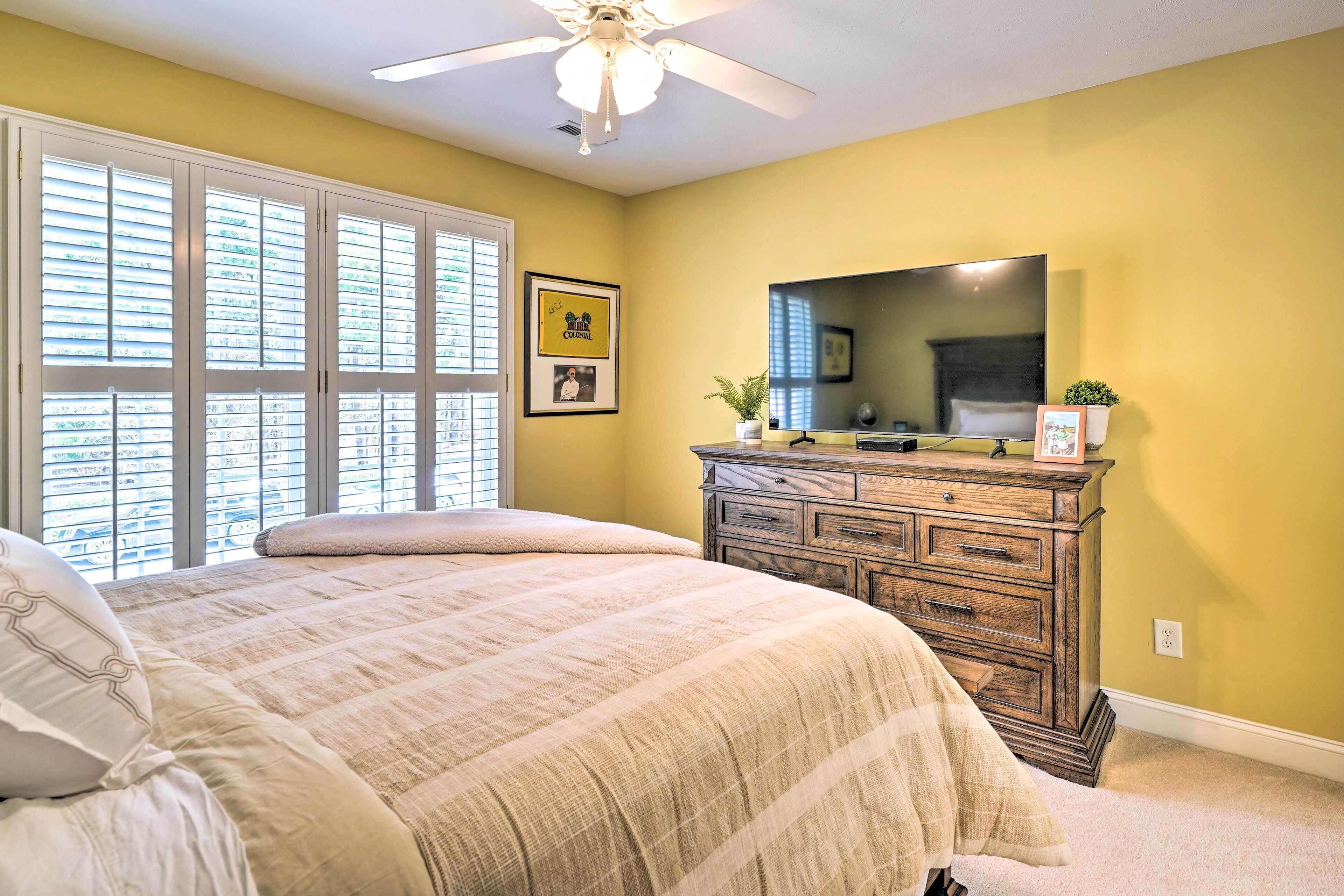 A bedroom with a bed, a dresser, a mirror, and a ceiling fan.