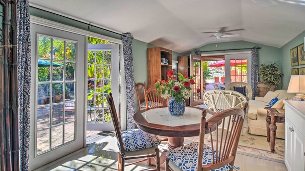 A sunlit dining area with a round table, chairs, and a vase of flowers.