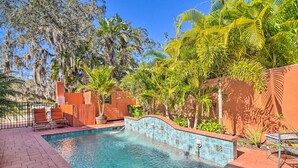 A swimming pool with tiled walls, surrounded by palm trees and a brick patio.