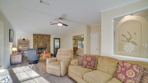 A living room with a beige sofa, a black chair, a fireplace, and a ceiling fan. - Stanardsville Cabin Rental ~ 24 Mi to Shenandoah! (Stanardsville)