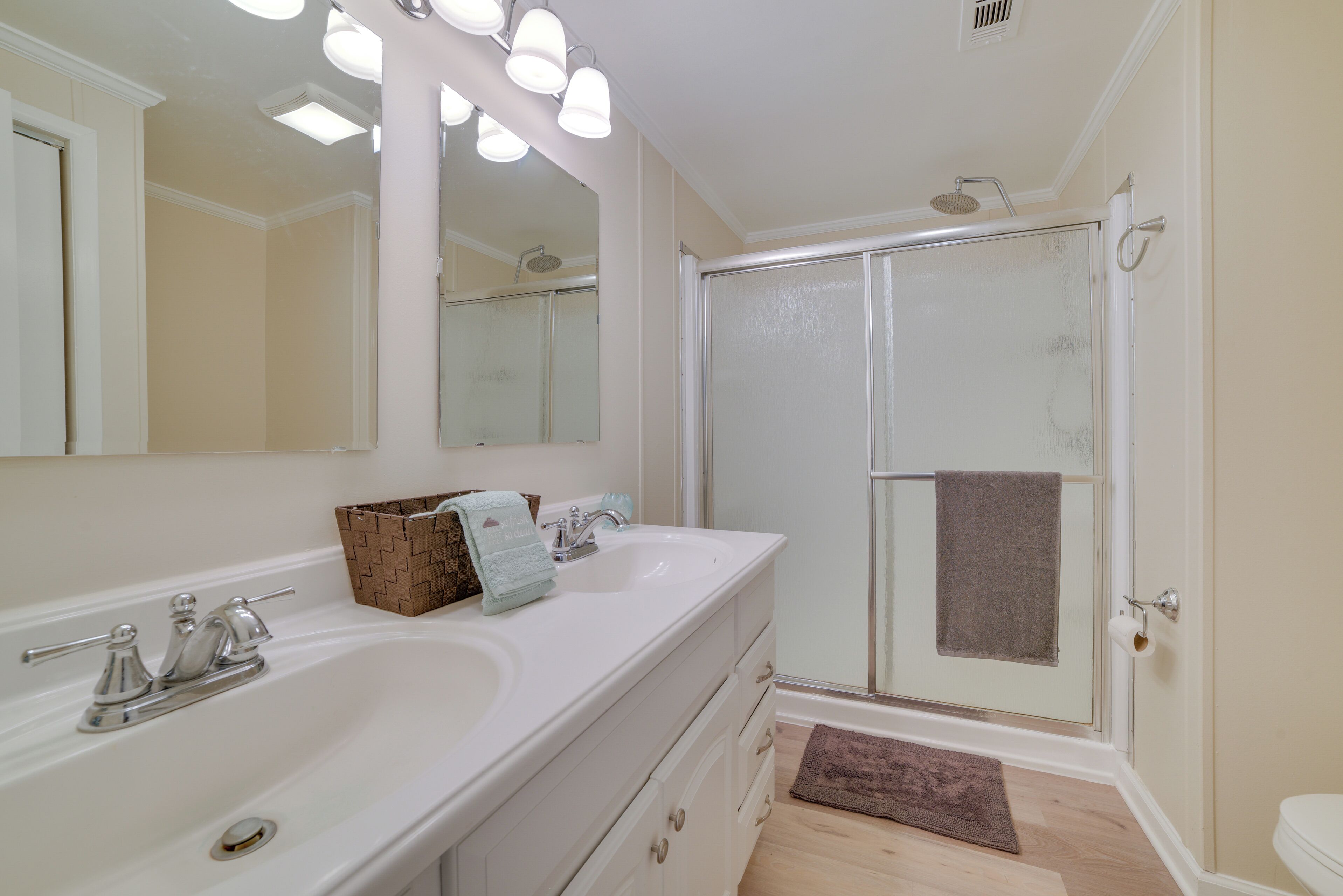 A bathroom with a double sink, a mirror, a shower, and a towel rack.