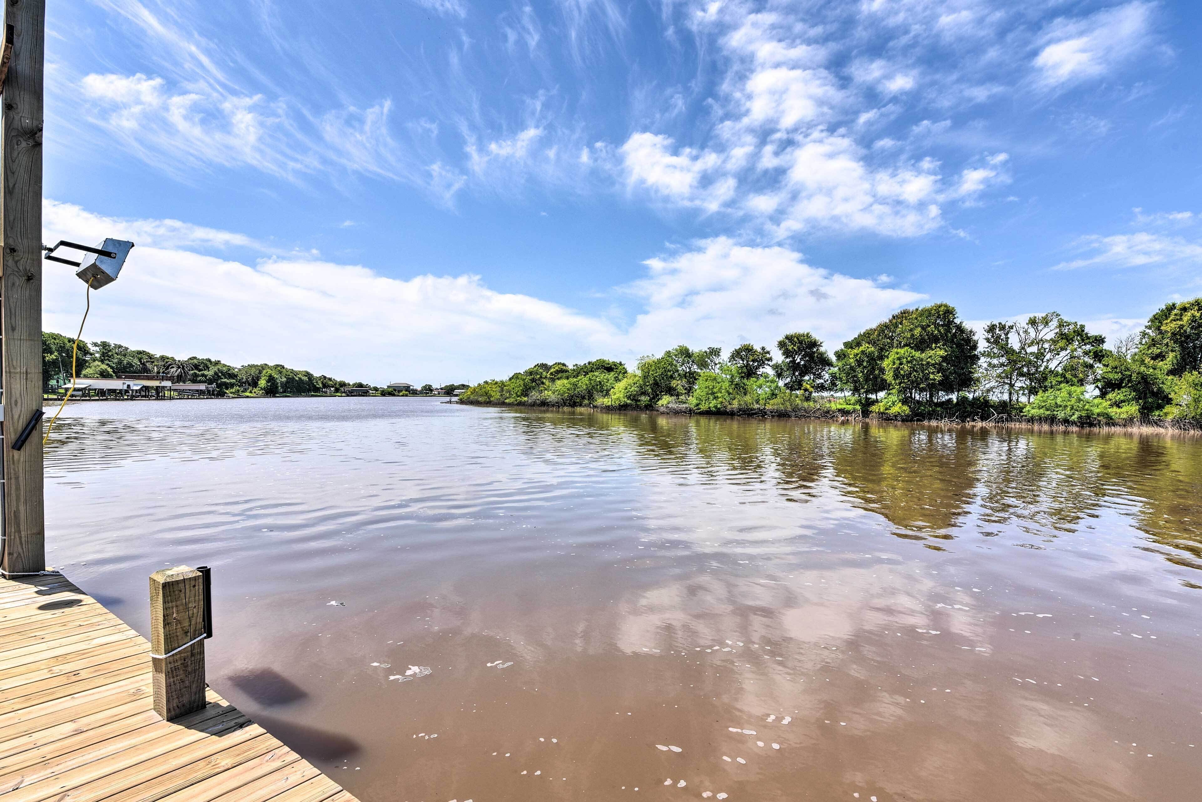 A wooden dock extending into a calm river with a clear sky and trees in the background.