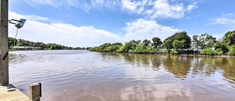 A wooden dock extending into a calm river with a clear sky and trees in the background.