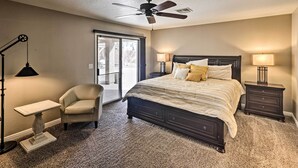 A bedroom with a bed, a chair, a desk, a ceiling fan, and a nightstand with a lamp.