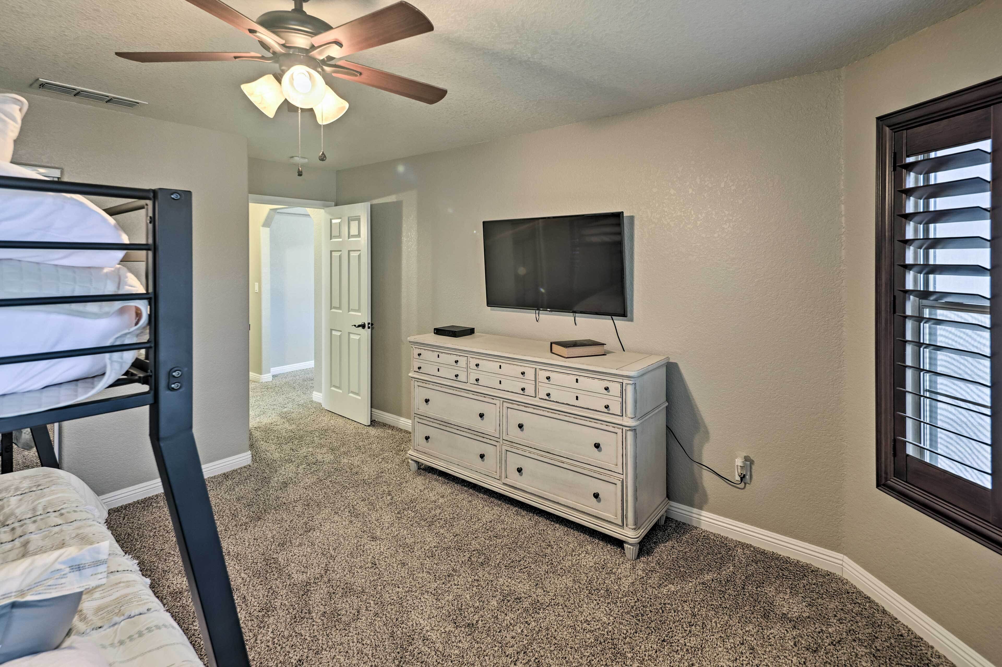 A bedroom with a bunk bed, a dresser, a television, and a ceiling fan.