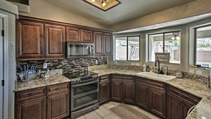 A kitchen with dark wooden cabinets, granite countertops, stainless steel appliances, and a large window providing natural light.