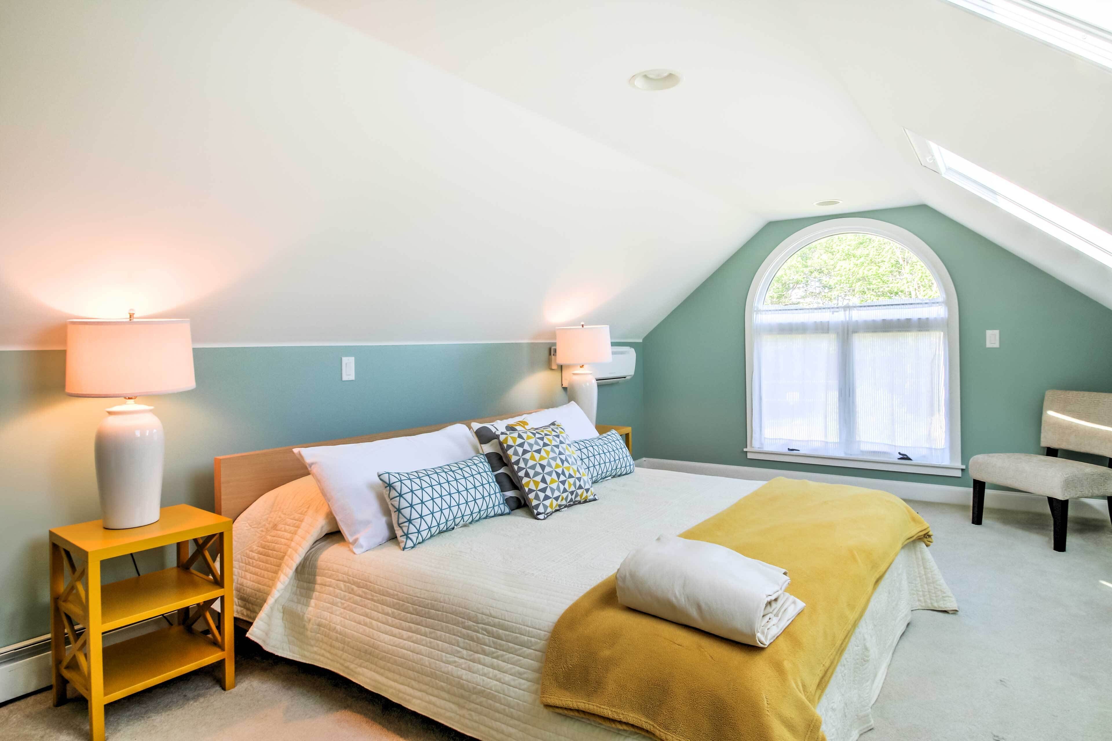 A bedroom with a bed, two bedside lamps, a bench, and a window with a view.