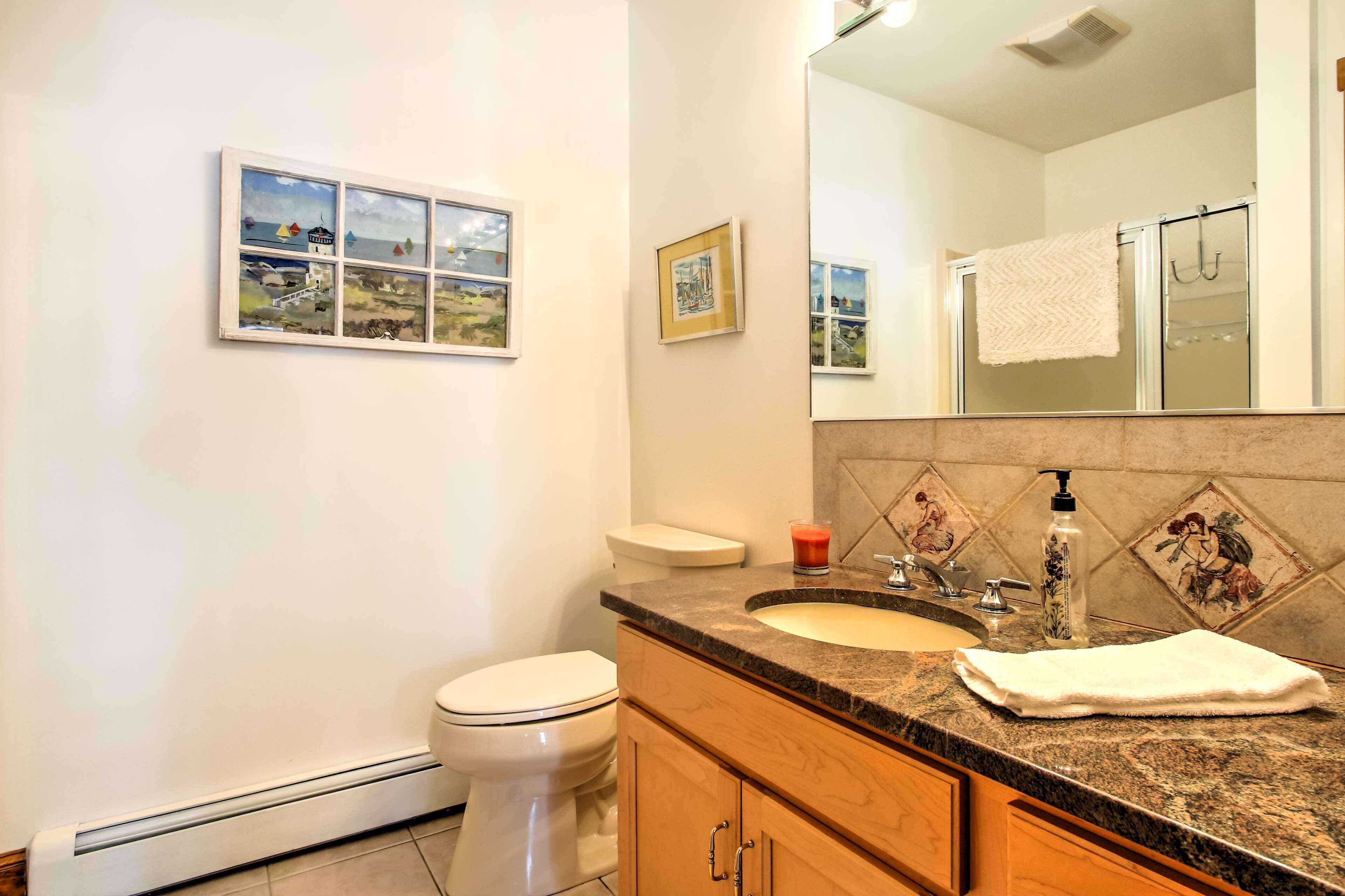 A bathroom with a toilet, sink, and mirror. There are framed pictures on the wall.