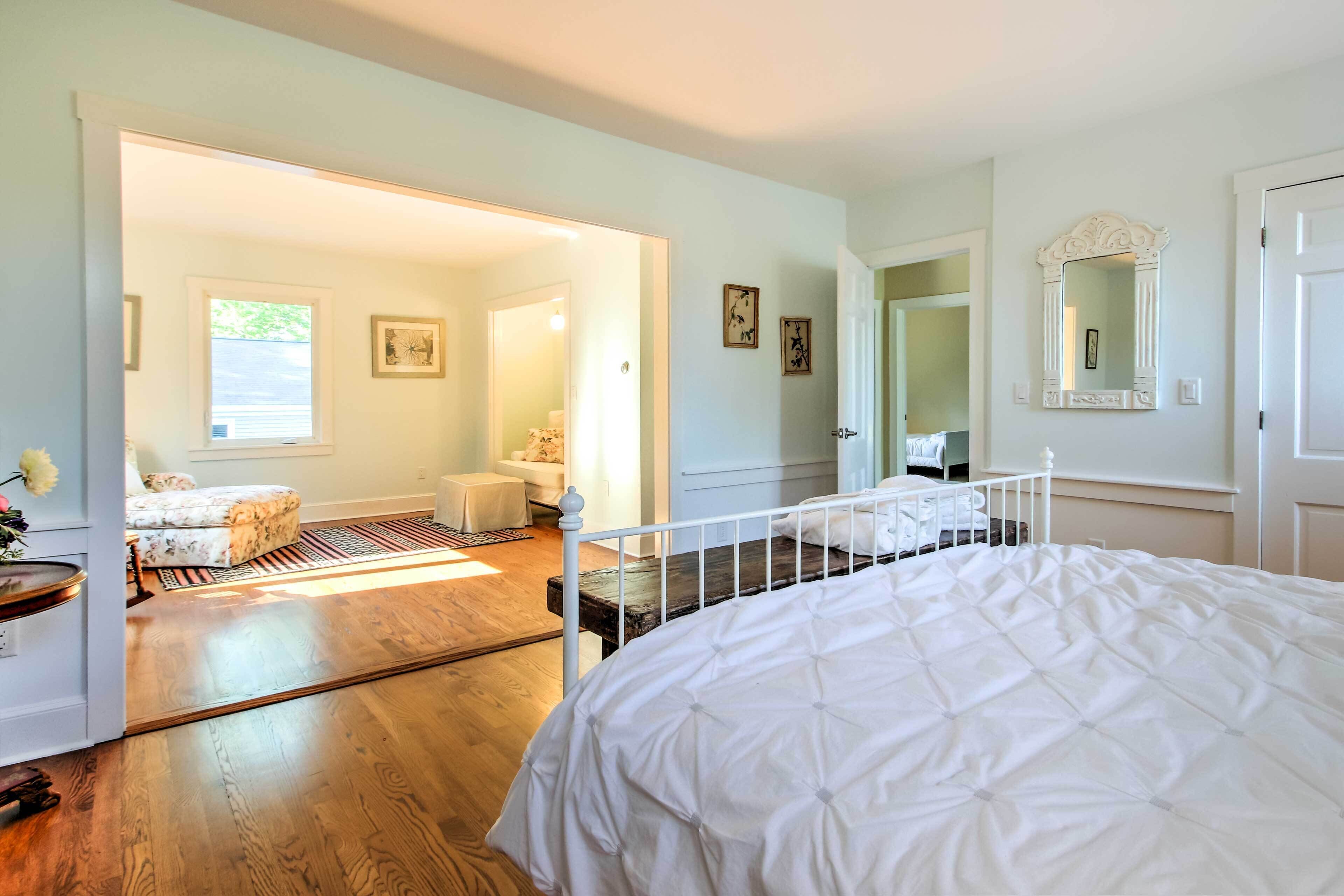 Un dormitorio con una cama grande, suelo de madera, una puerta blanca y un pasillo que conduce a un baño.