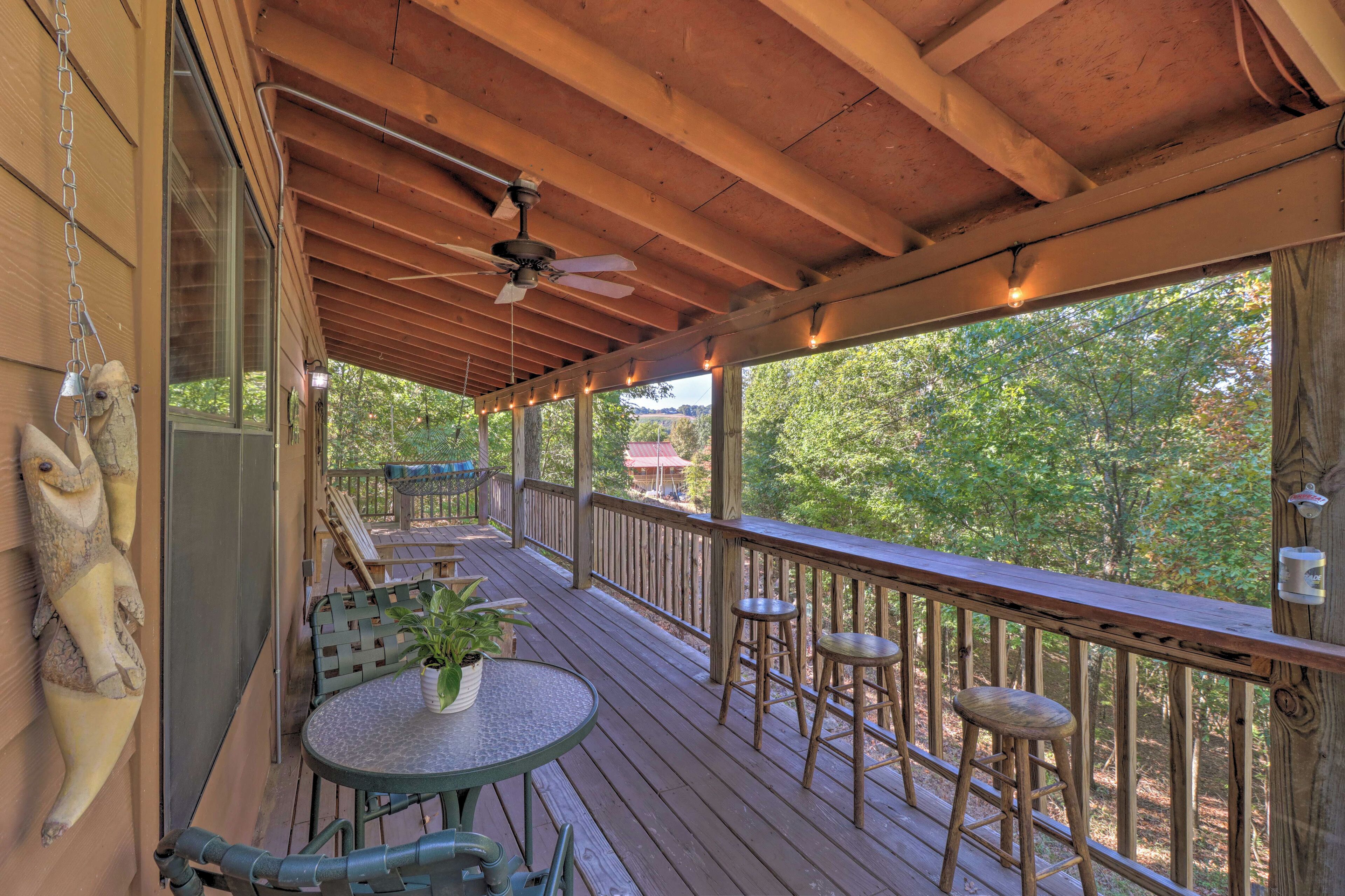 A wooden deck with a table and chairs, a ceiling fan, and a view of trees.