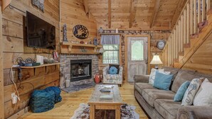 A cozy log cabin interior with a stone fireplace, wooden walls, a television, and a comfortable seating area. - Secluded Sevierville Cabin w/ Hot Tub! (Sevierville)