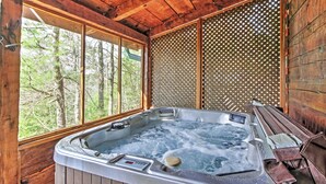 A wooden cabin with a hot tub, large windows, and a view of trees. - Secluded Sevierville Cabin w/ Hot Tub! (Sevierville)