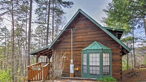 A wooden cabin with a green roof, a covered porch, and a window with shutters. - Secluded Sevierville Cabin w/ Hot Tub! (Sevierville)