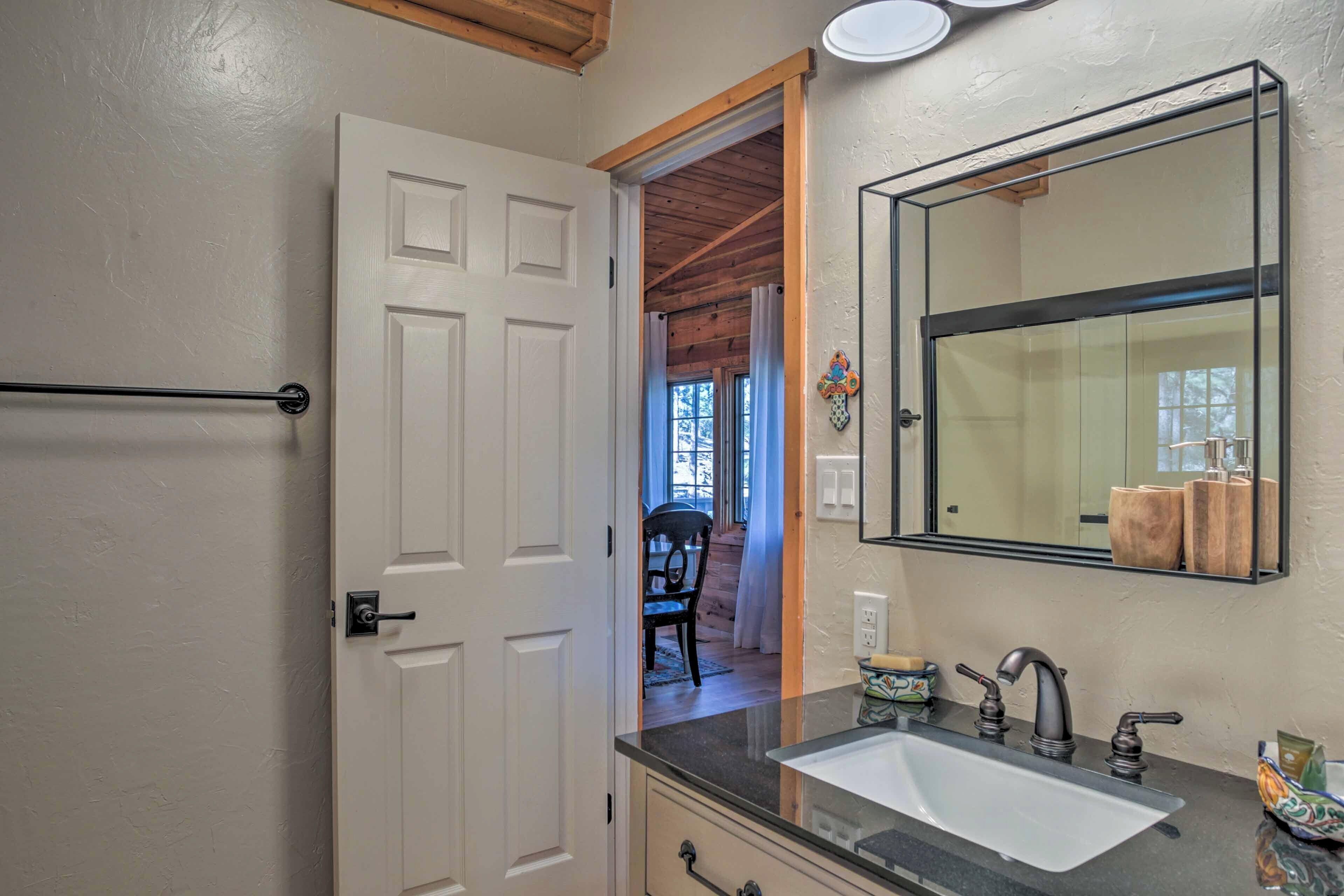 A bathroom with a white door, a black countertop sink, and a mirror above it.