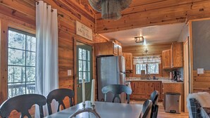 A wooden cabin interior with a dining table, chairs, a chandelier, and a kitchen area. - Ruidoso Log Cabin Retreat - Peaceful & Convenient (Ruidoso)