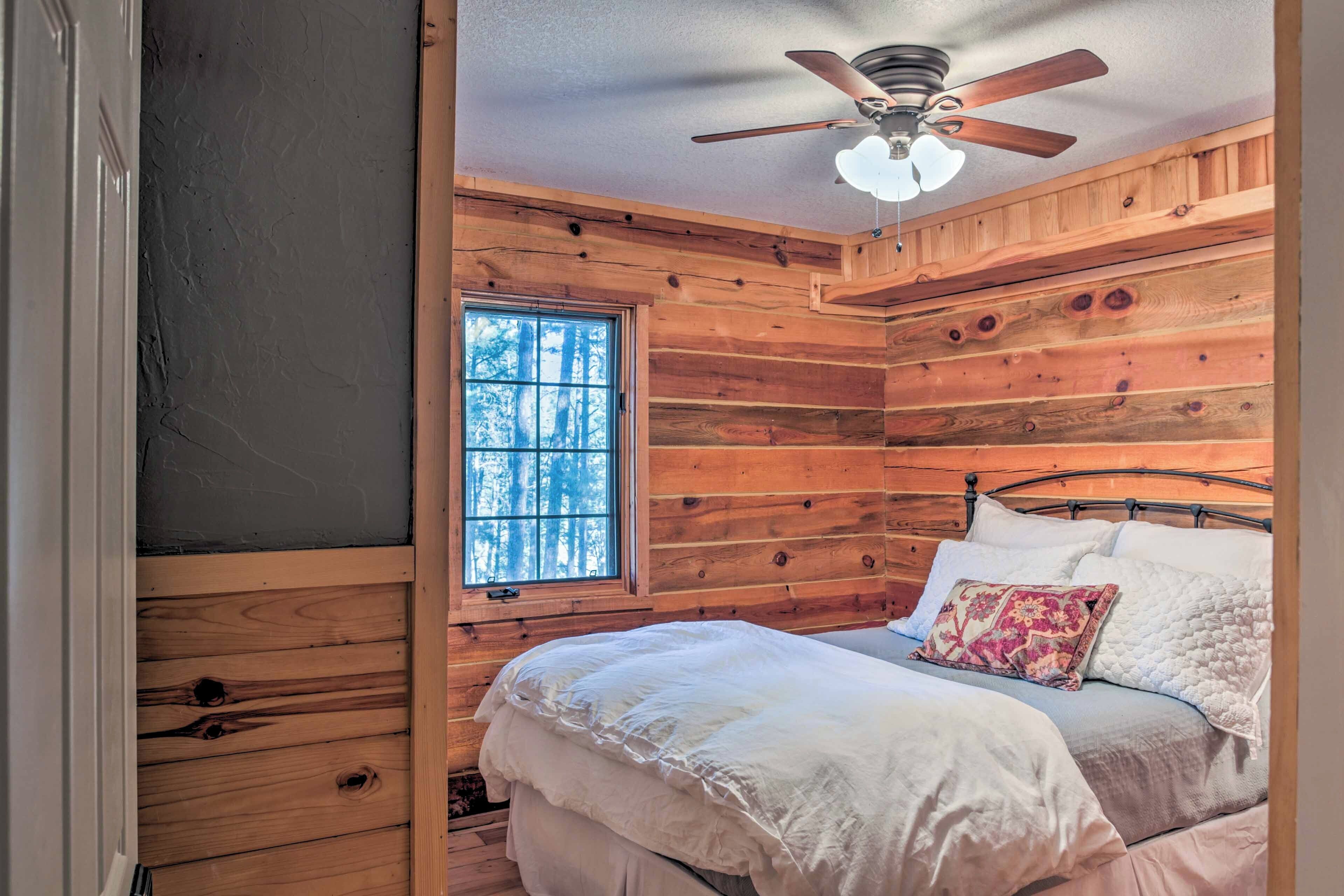 A wooden cabin bedroom with a bed, pillows, a ceiling fan, and a window.