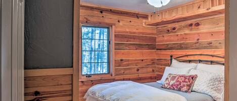 A wooden cabin bedroom with a bed, pillows, a ceiling fan, and a window.