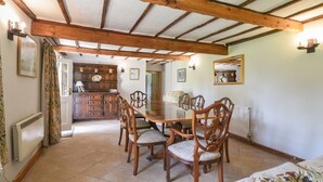 A dining area with a wooden table and chairs, a kitchen in the background, and a mirror on the wall. - Millwater Cottage (Axminster)