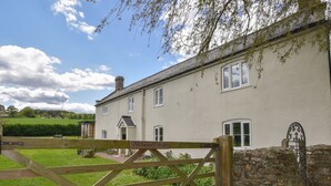 A cottage with a wooden gate labeled "Millwater Cottage," stone wall, and a grassy yard. - Millwater Cottage (Axminster)