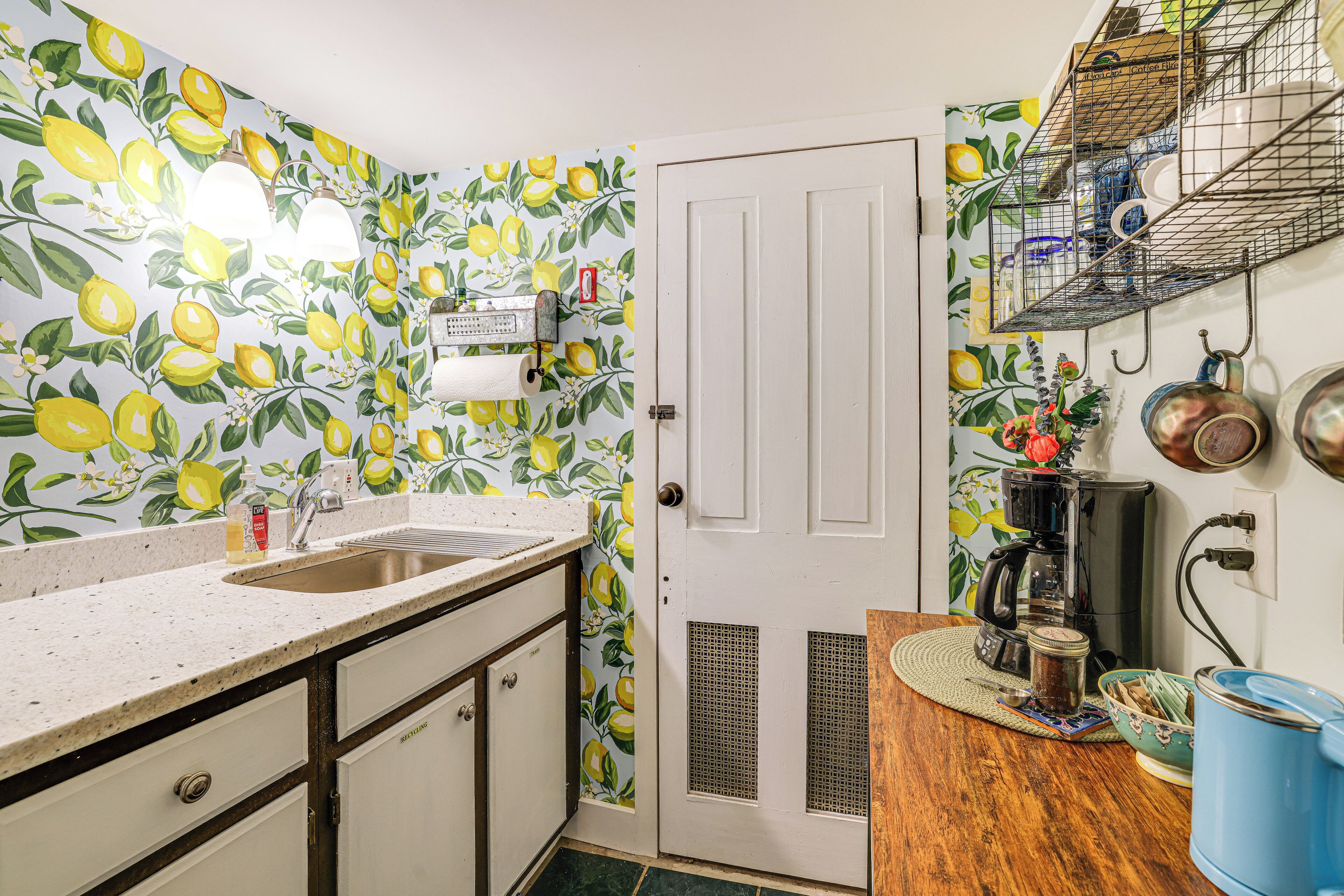 A kitchen with a lemon-themed wallpaper, a sink, cabinets, and a coffee maker on the counter.