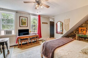 Une chambre à coucher avec un lit, un bureau, une télévision et une fenêtre avec des rideaux.