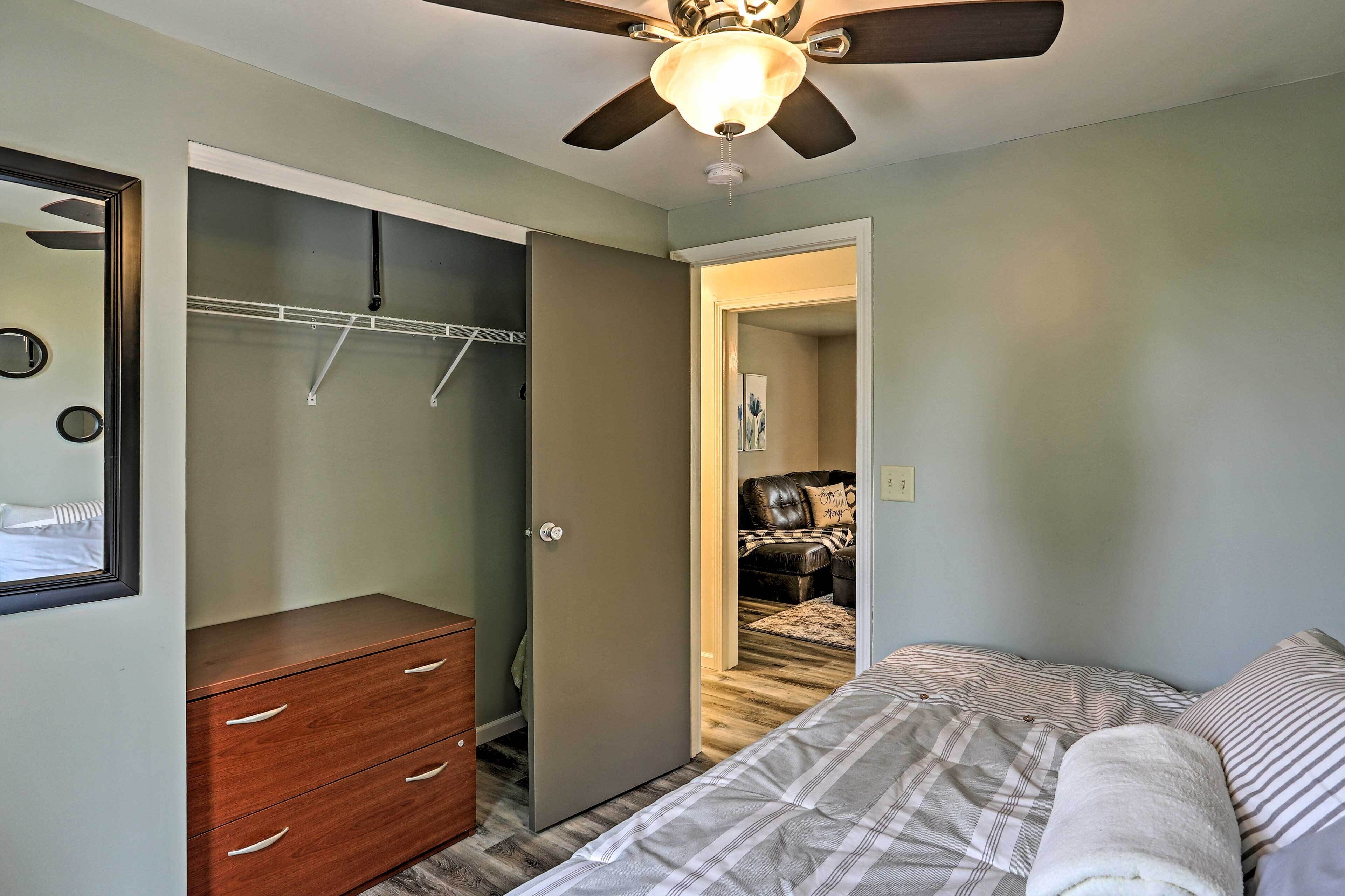 A bedroom with a bed, a wooden dresser, a closet with hanging space, and a ceiling fan.