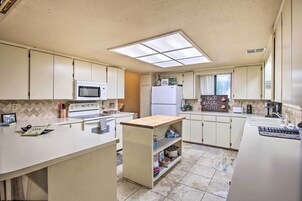Una cocina con armarios blancos, microondas, refrigerador y una pequeña isla con estantes.