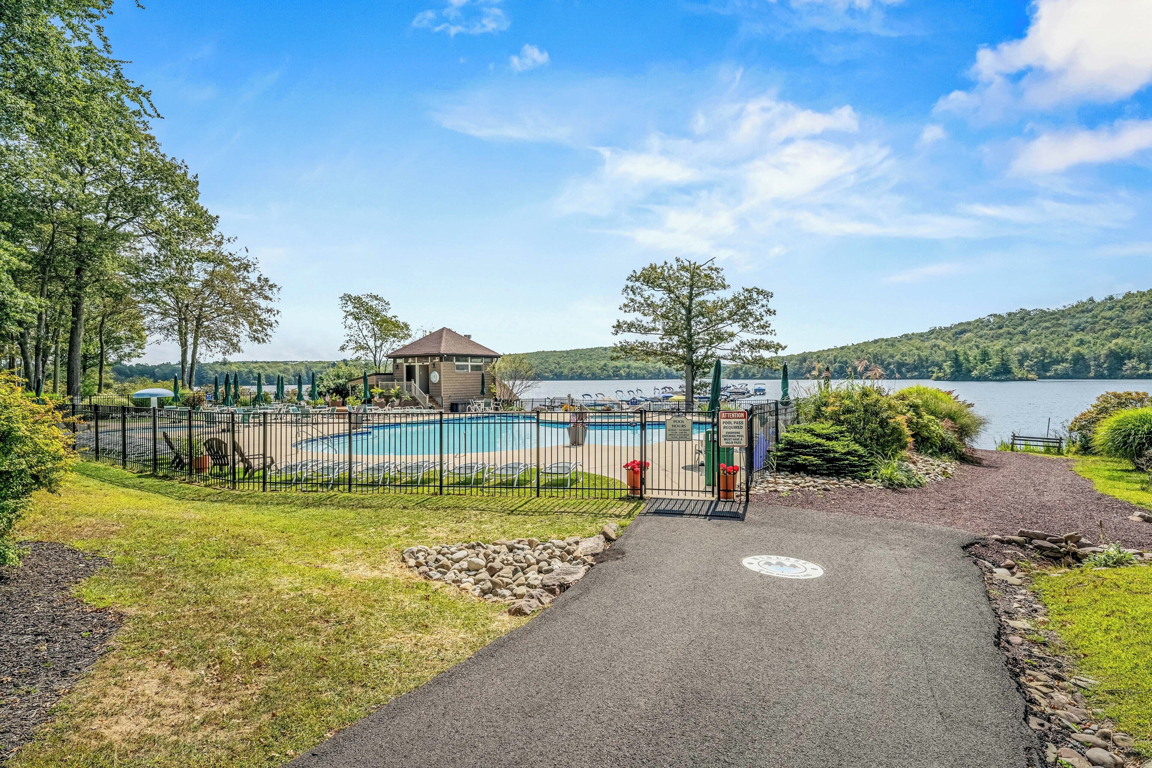 A swimming pool area with a pathway leading to it, surrounded by trees and a view of a lake.