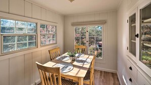 A dining area with a wooden table and chairs, a ceiling light fixture, and windows with views of trees and a house. - Wine Country Escape w/ Hot Tub in River Pines! (River Pines)