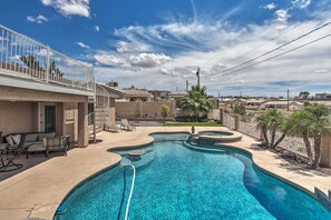 A swimming pool with a curved design, surrounded by a patio area with outdoor furniture and a small garden.