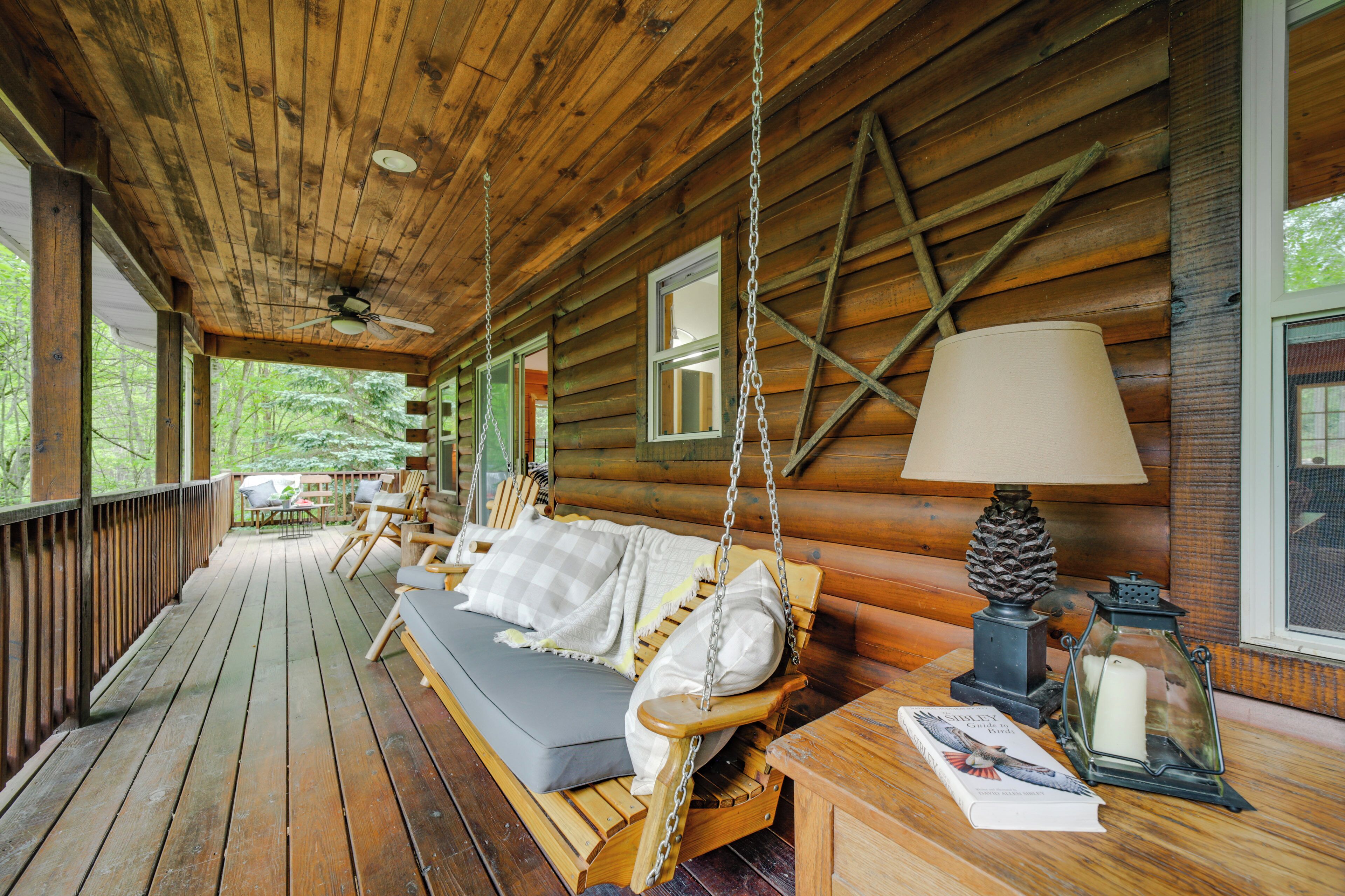 A wooden cabin with a porch, a swing, a sofa, a table with a lamp, and a lantern.