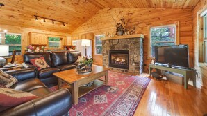 Interior acogedor de una cabaña con chimenea de piedra, asientos de cuero y televisor.