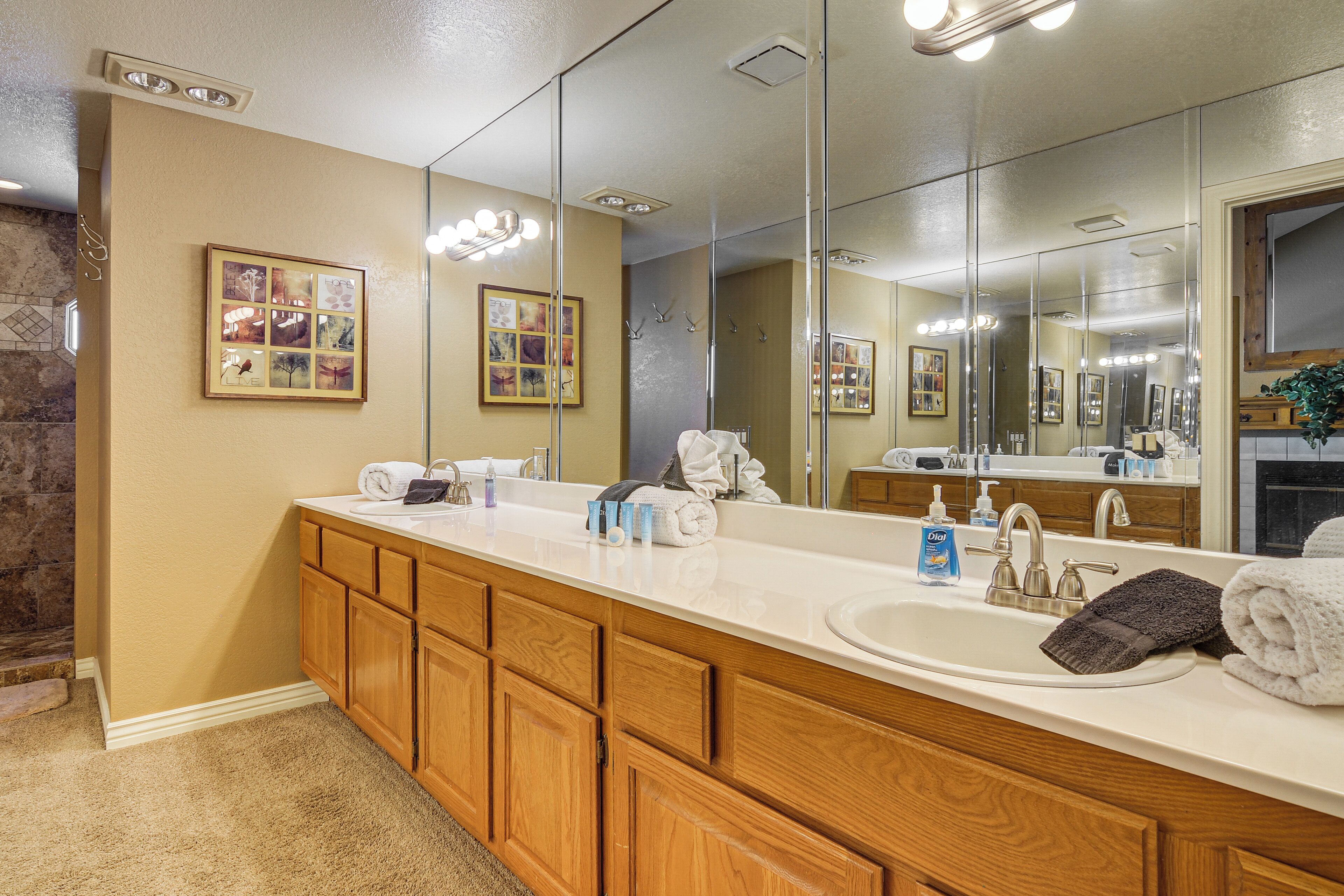 A bathroom with a large mirror, wooden cabinets, a sink, and a shower area.