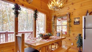 Eine Holzhütte mit Innenraum, einem Esstisch mit Stühlen, einer Bank, einer Chandelüster und einem Kühlschrank.